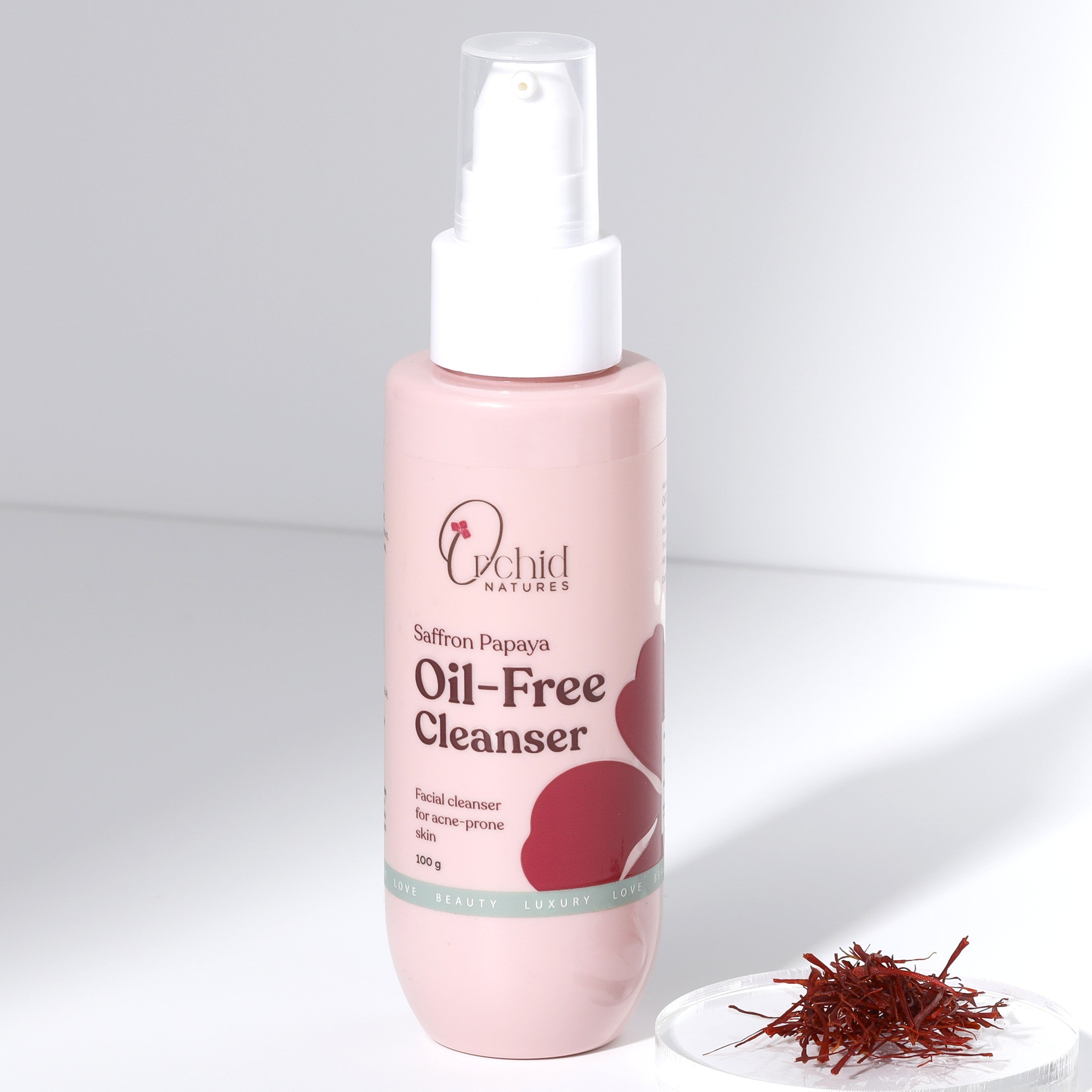 Pink bottle of Saffron Papaya Oil-Free Cleanser with saffron strands on a white background