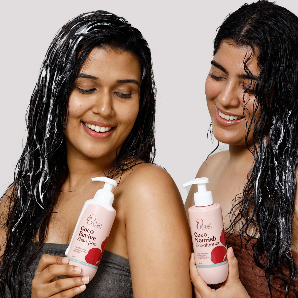 Two women with wet hair holding Coco Revive shampoo and conditioner bottles against a plain background.
